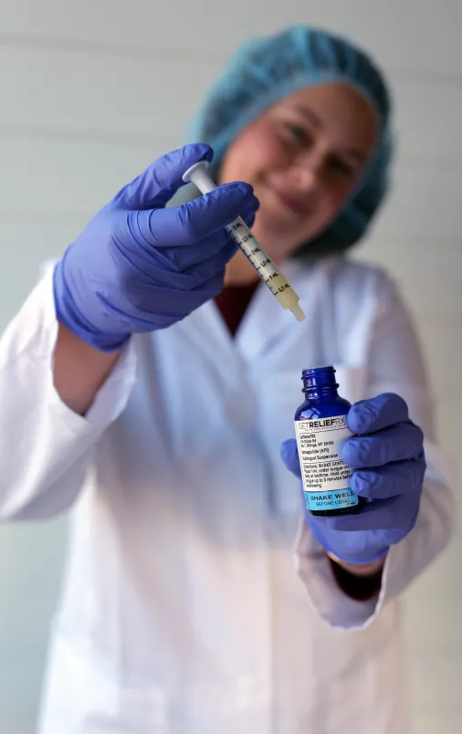 A woman in a lab coat, and gloves holds a bottle of medicine.